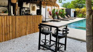 A poolside area with a bar, lounge chairs, and a thatched-roof structure. - Abode Hua Hin (Hua Hin)
