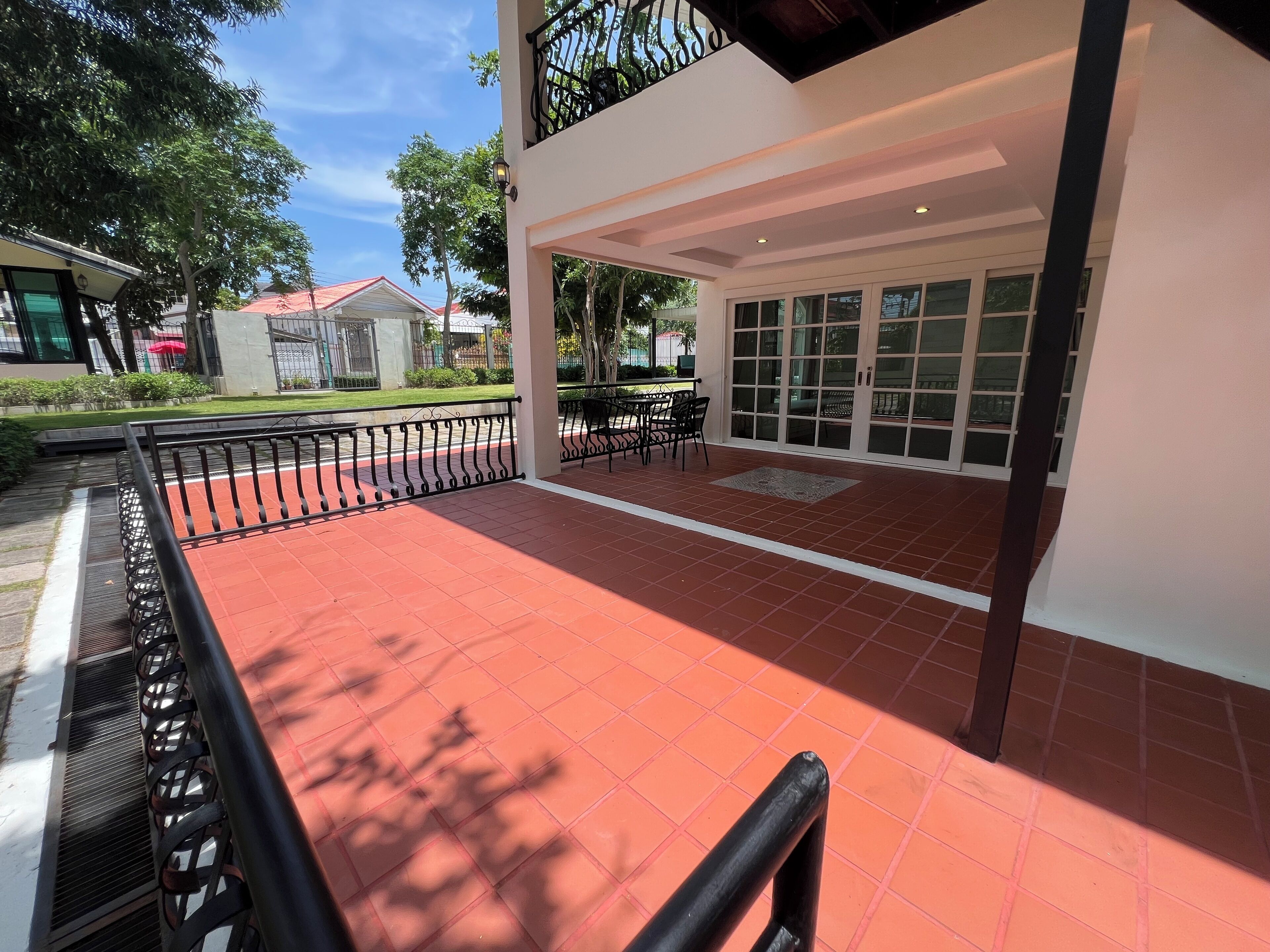 A covered outdoor area with a red-tiled floor, black metal railings, and a glass door leading to an interior space.