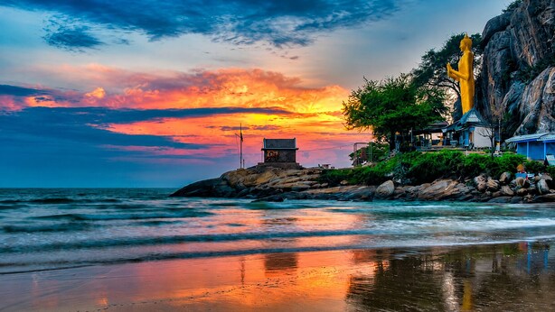 A coastal scene with a large golden statue, a small building, and a rocky shoreline. - Abode Hua Hin (Hua Hin)