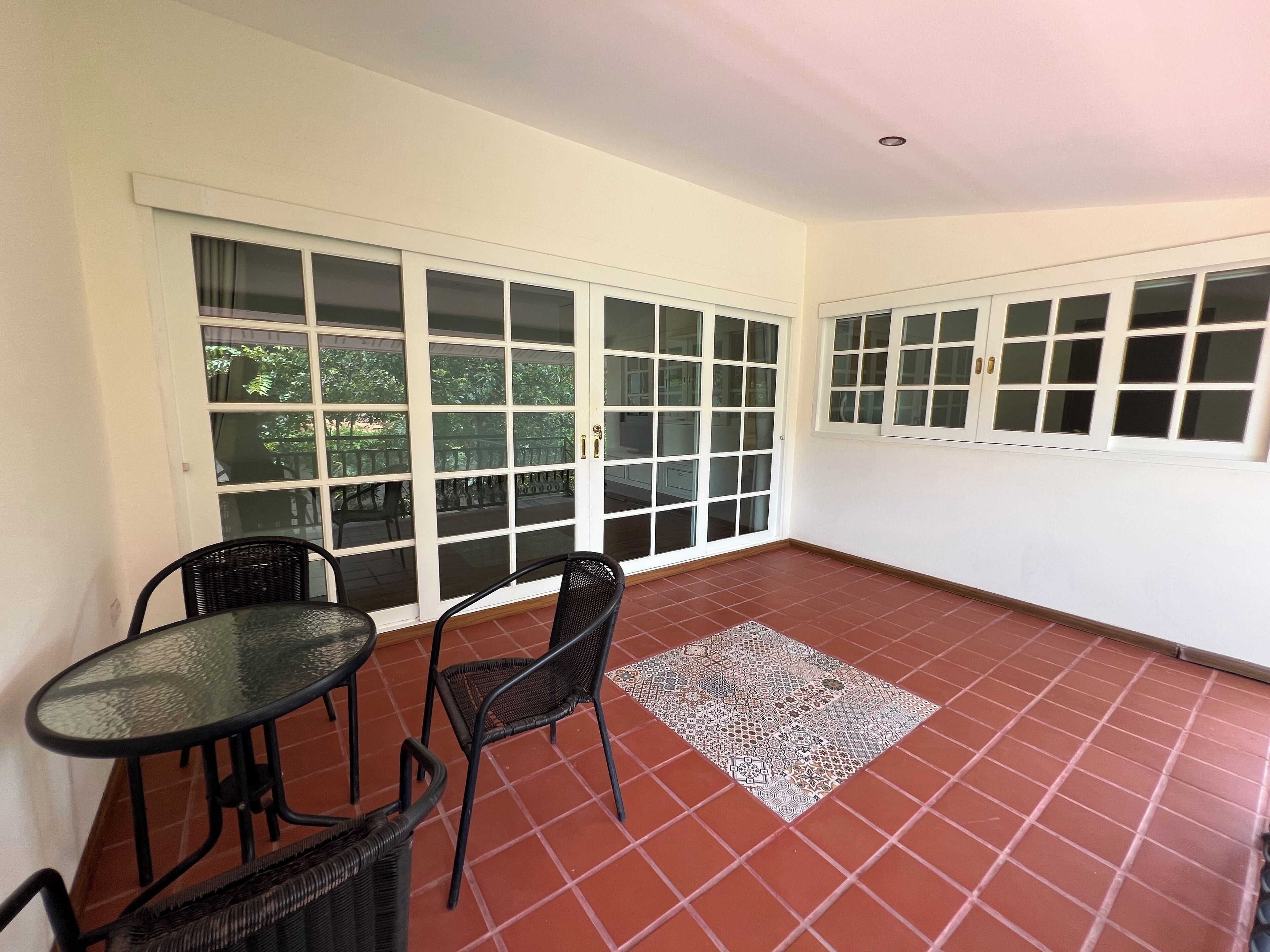 A room with a tiled floor, a glass table, two wicker chairs, and a sliding glass door leading to an outdoor area.