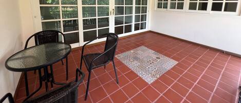 A room with a tiled floor, a glass table, two wicker chairs, and a sliding glass door leading to an outdoor area.