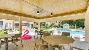 A covered outdoor area with tables and chairs, a pool, and a flamingo float.