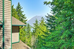 Un bâtiment en bois, orné de boiseries vertes, entouré d’un feuillage dense et verdoyant, avec une montagne en arrière-plan.