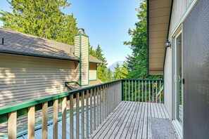 Une terrasse en bois avec une rambarde verte, un porche abrité et une vue sur les arbres et les montagnes en arrière-plan.