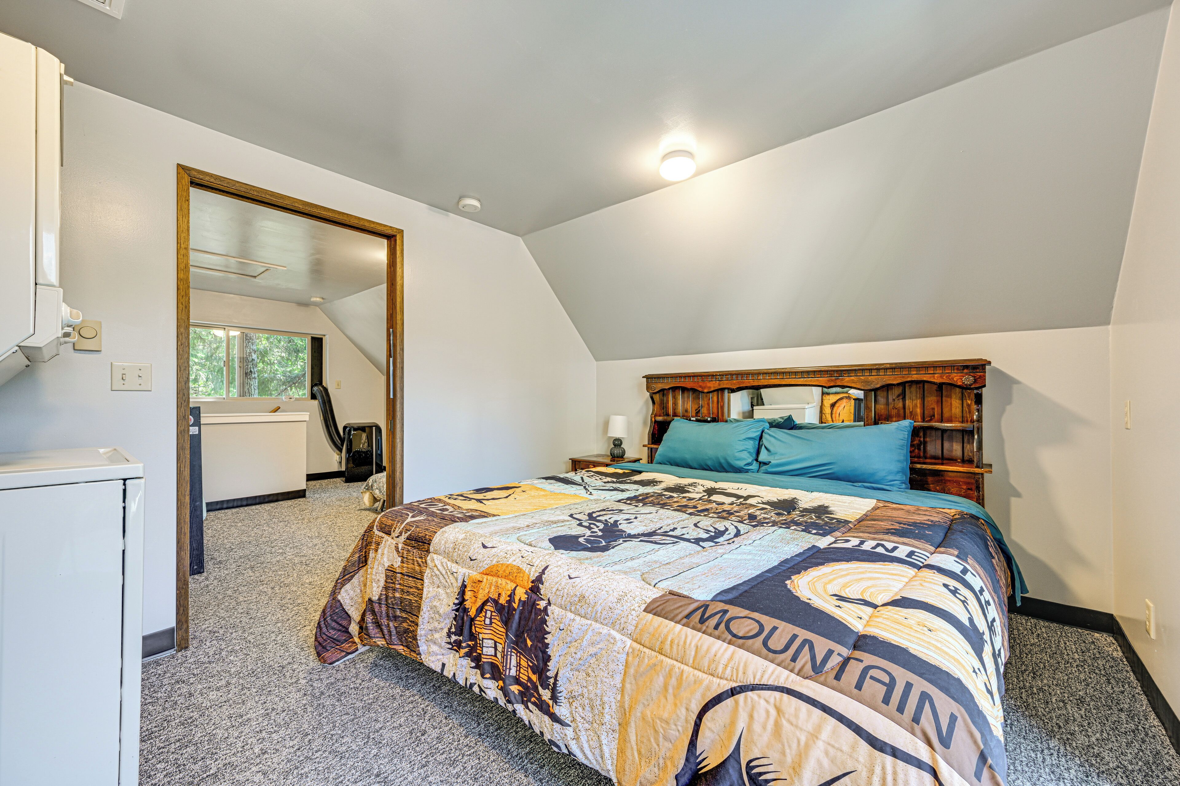 A bedroom with a large bed, a wooden headboard, a mirror, and a door leading to another room.