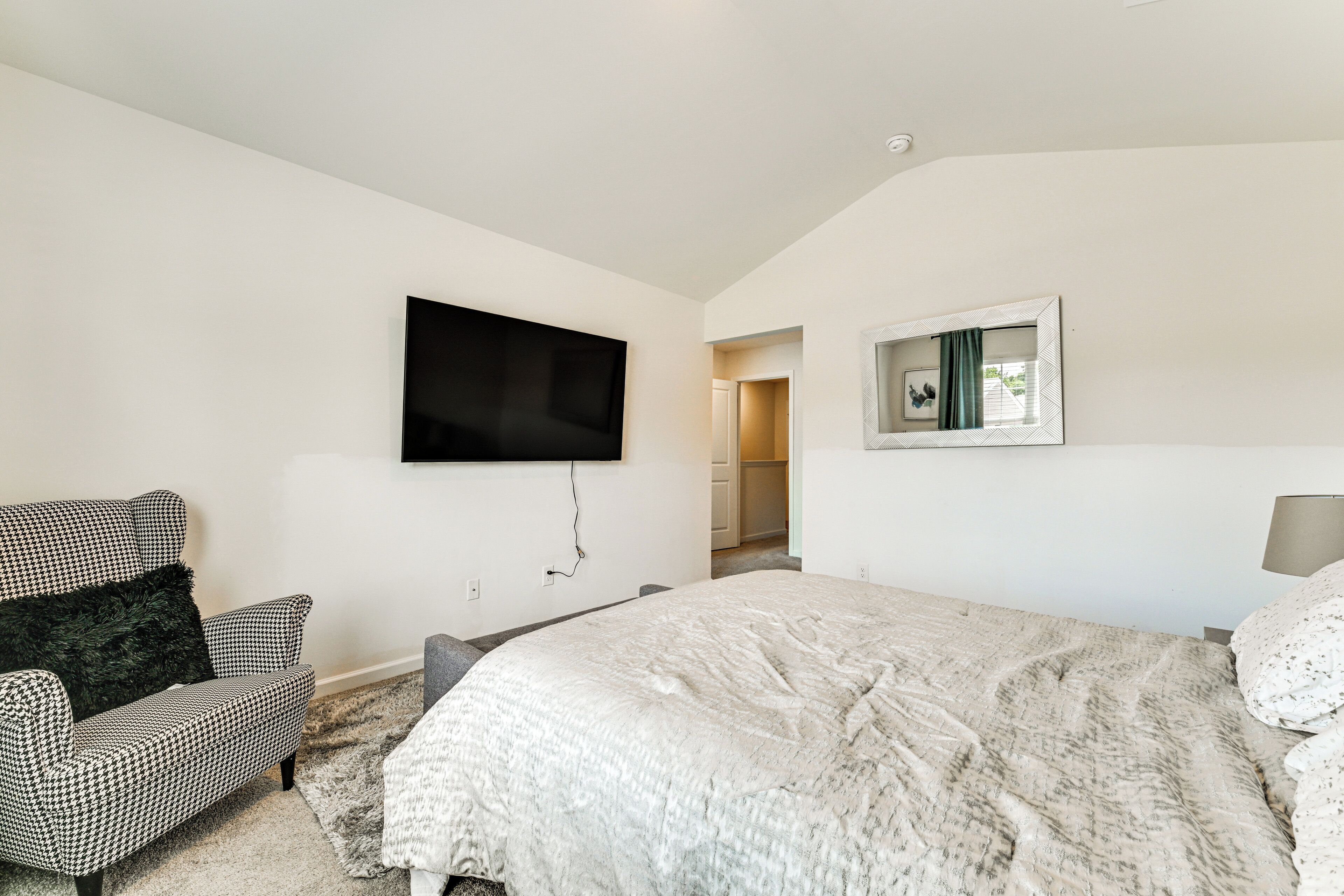 A bedroom with a large bed, a television mounted on the wall, a chair, and a mirror.