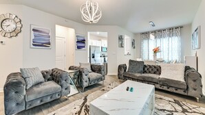Ein modernes Wohnzimmer mit zwei grauen, gesteppten Sofas, einem weißen Marmortisch und einer Kristallleuchtre.