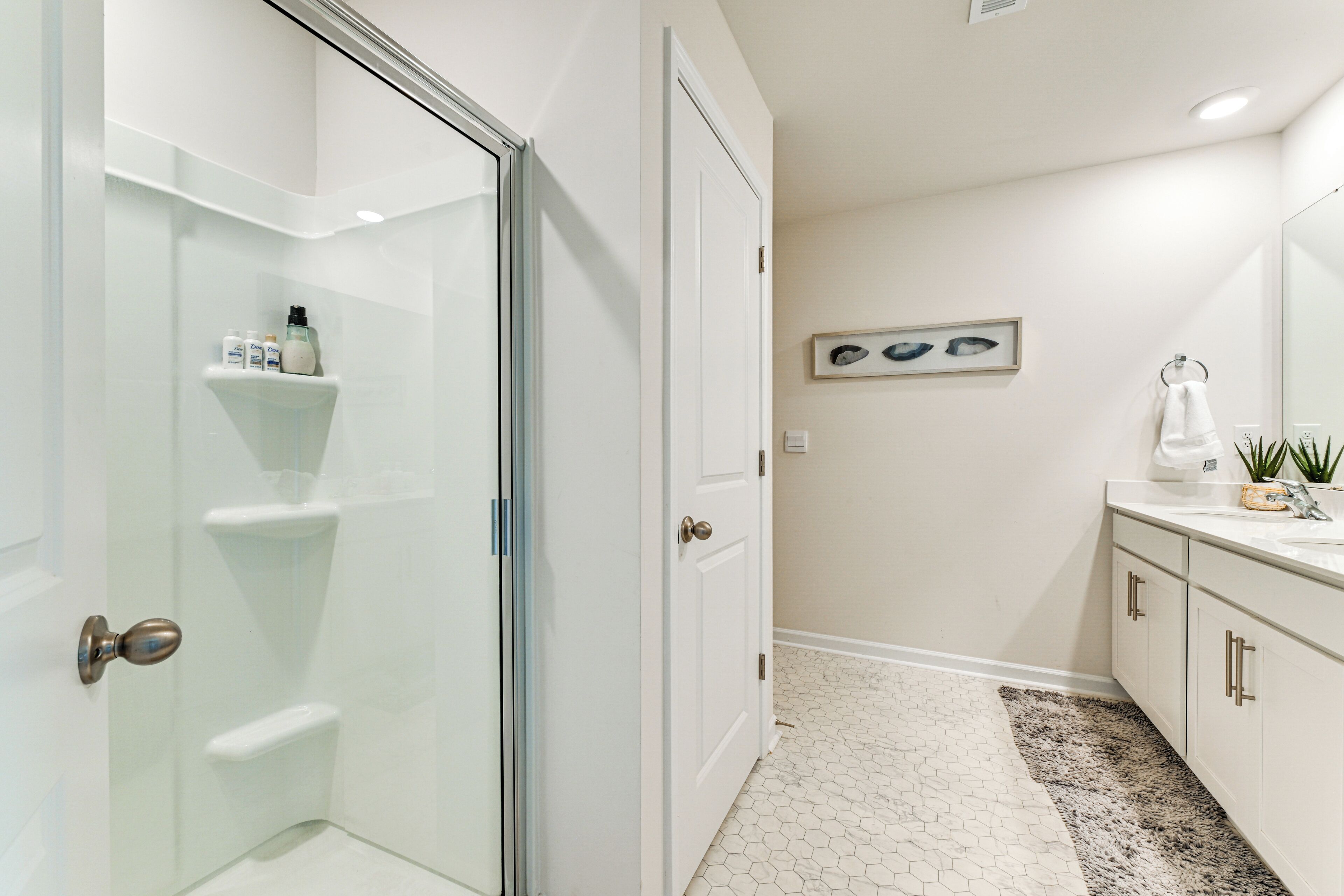 A modern bathroom with a glass shower enclosure, a white vanity with a sink, and a hexagonal tile floor.