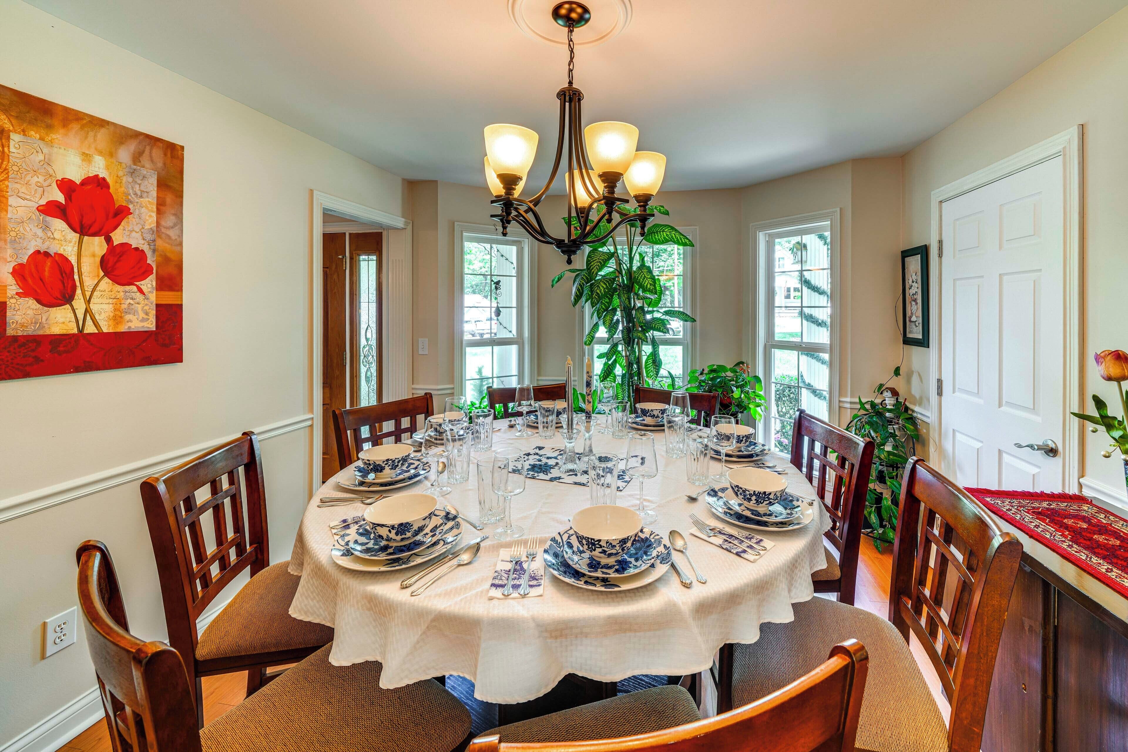 A dining room with a round table set for six, surrounded by wooden chairs.