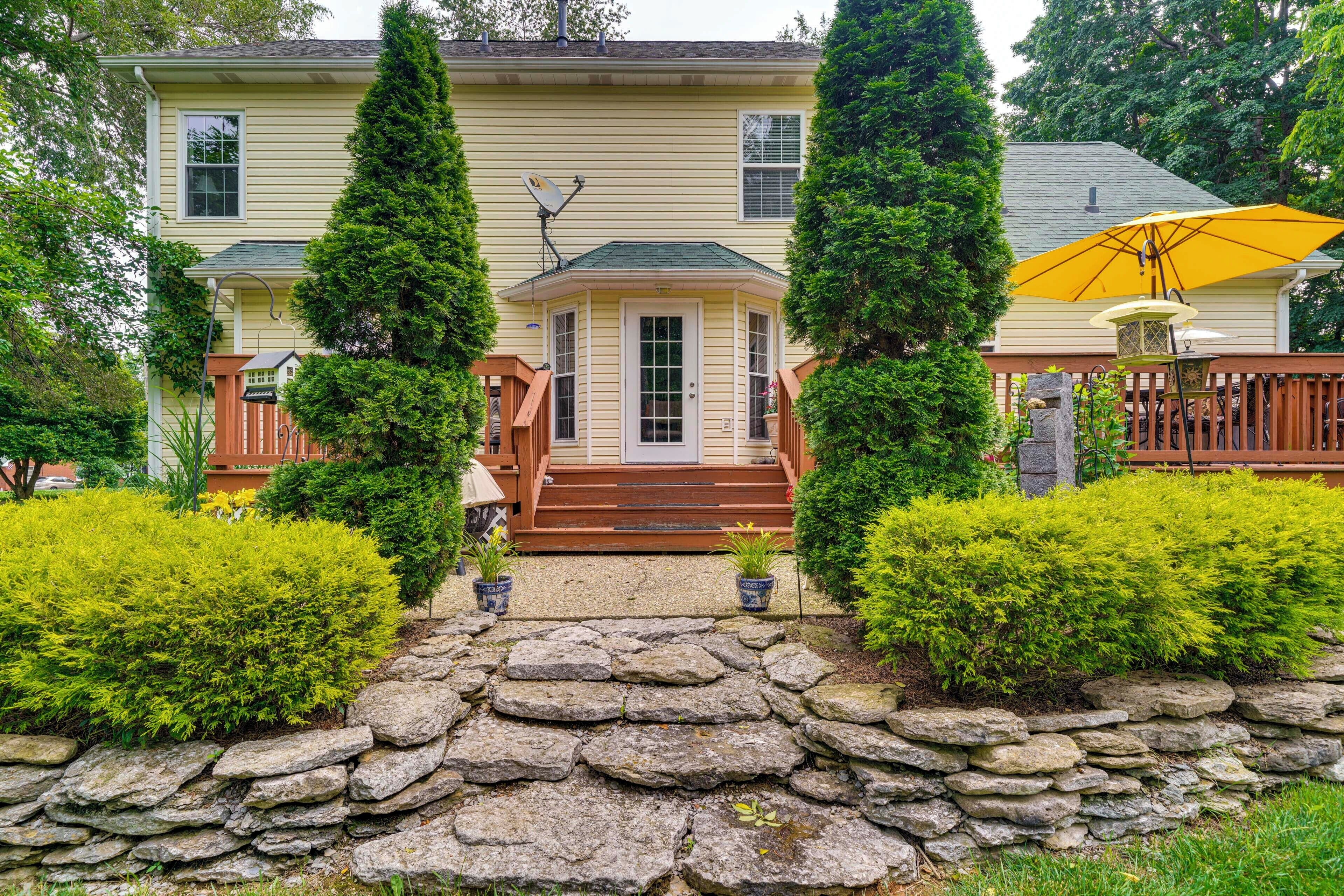 A two-story house with a stone pathway leading to the front door, surrounded by well-maintained bushes and a wooden fence.