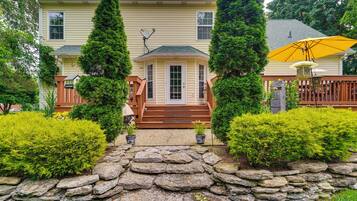 A two-story house with a stone pathway leading to the front door, surrounded by well-maintained bushes and a wooden fence.
