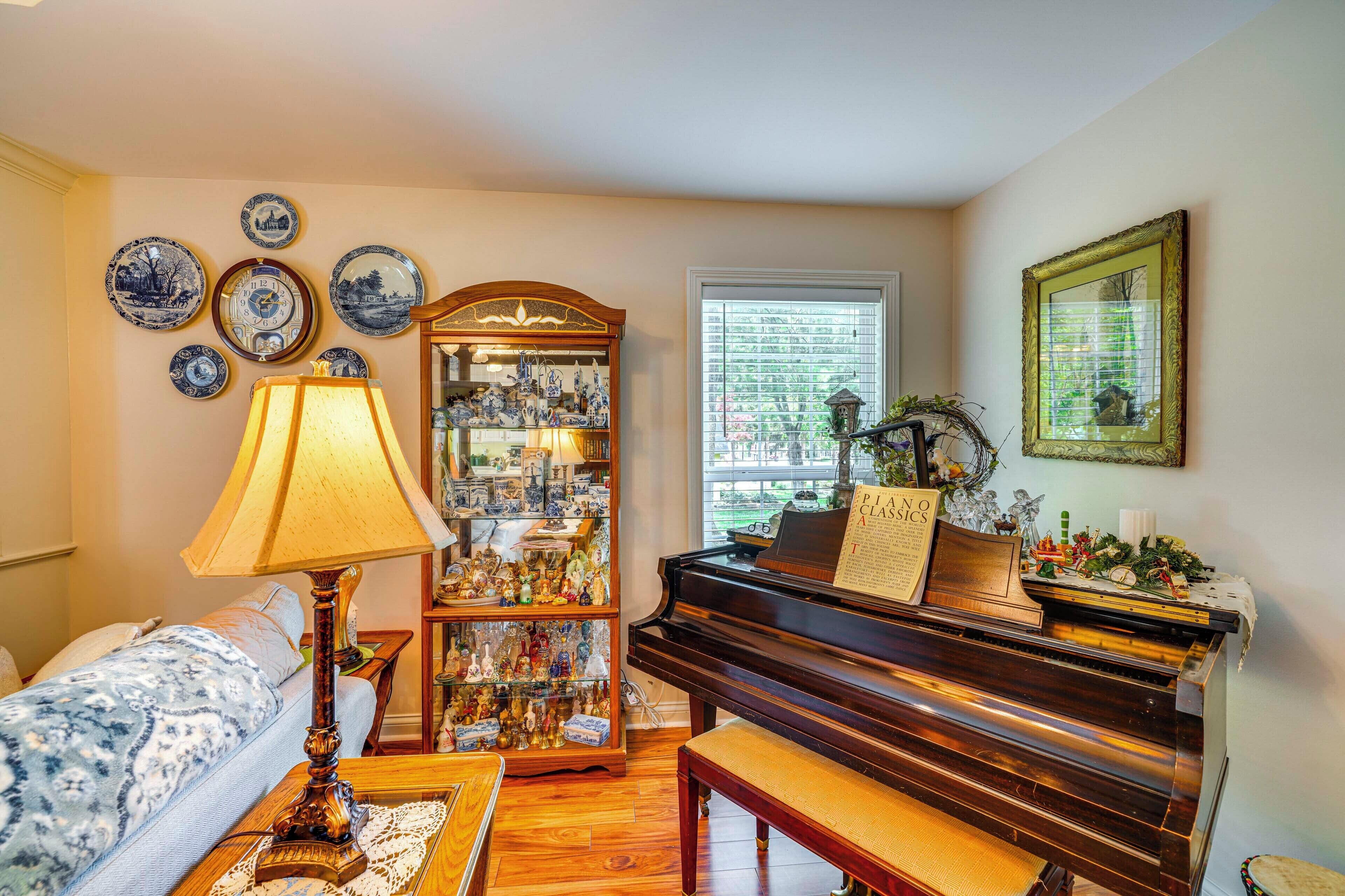 Un salon avec un piano, une lampe et une collection d’assiettes bleues et blanches accrochées au mur.