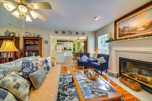A living room with a sofa, armchairs, a fireplace, a bookshelf, and a kitchen in the background. - 15 Mi to Louisville: Family Home w/ Private Yard! (Louisville)
