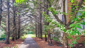 A pathway lined with trees and a brick building on the right. - 4 Mi to Dulles Airport: Spacious D.c. Area Home (Herndon)