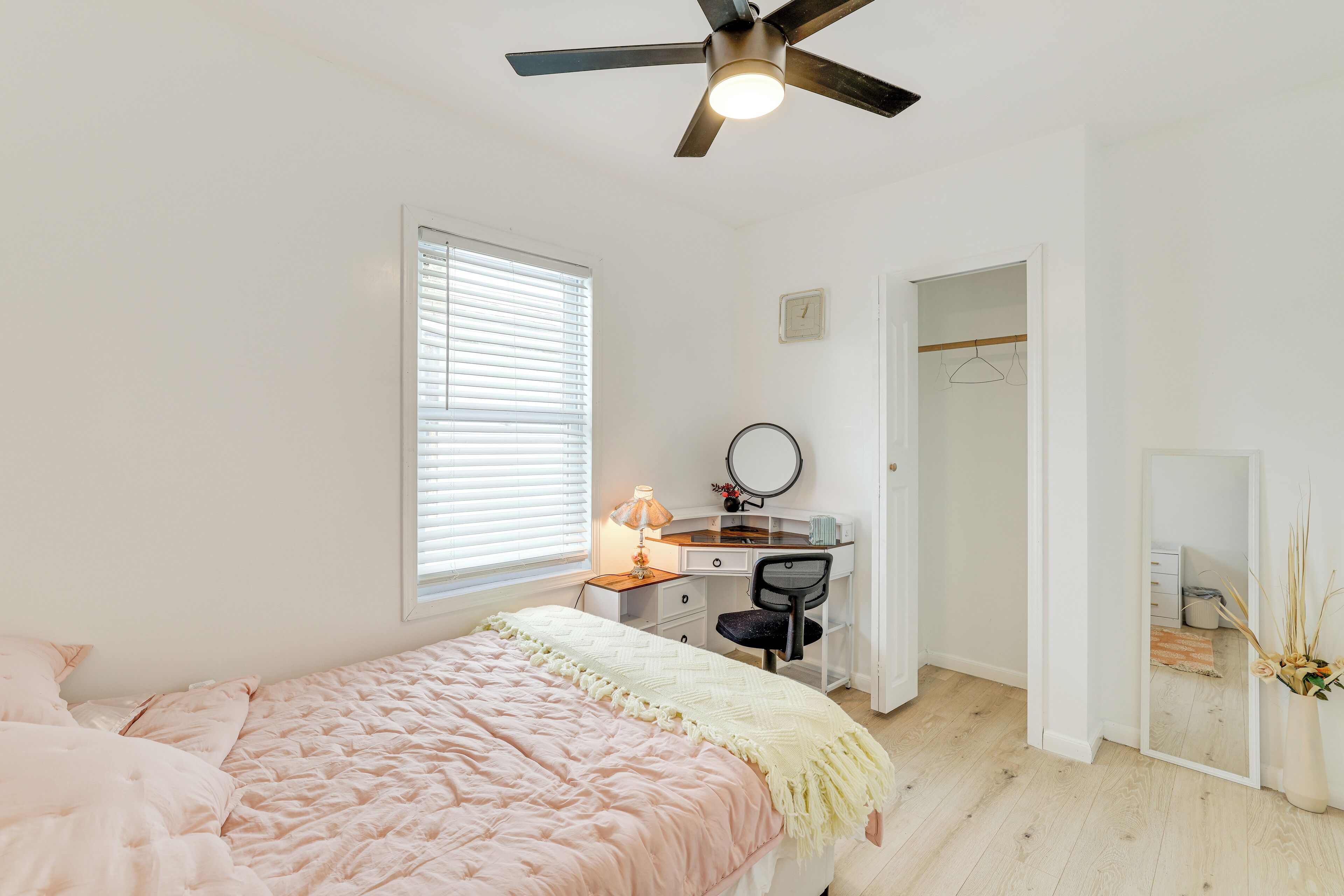 A bedroom with a bed, a desk, a chair, a mirror, and a ceiling fan.