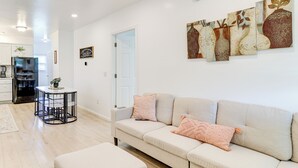 Una sala de estar moderna con un sofá color beige, una mesita redonda y una cocina al fondo.