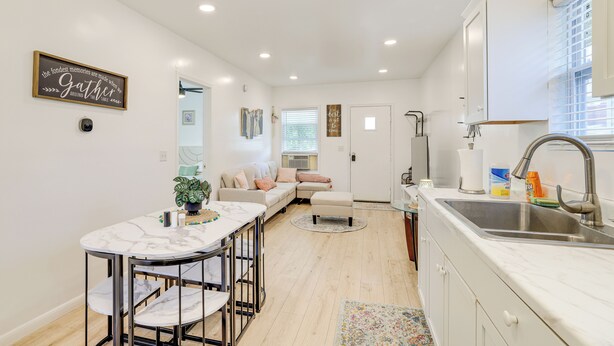 Una cocina moderna con encimera de mármol, un lavamanos y una zona de comedor con mesa y sillas blancas.