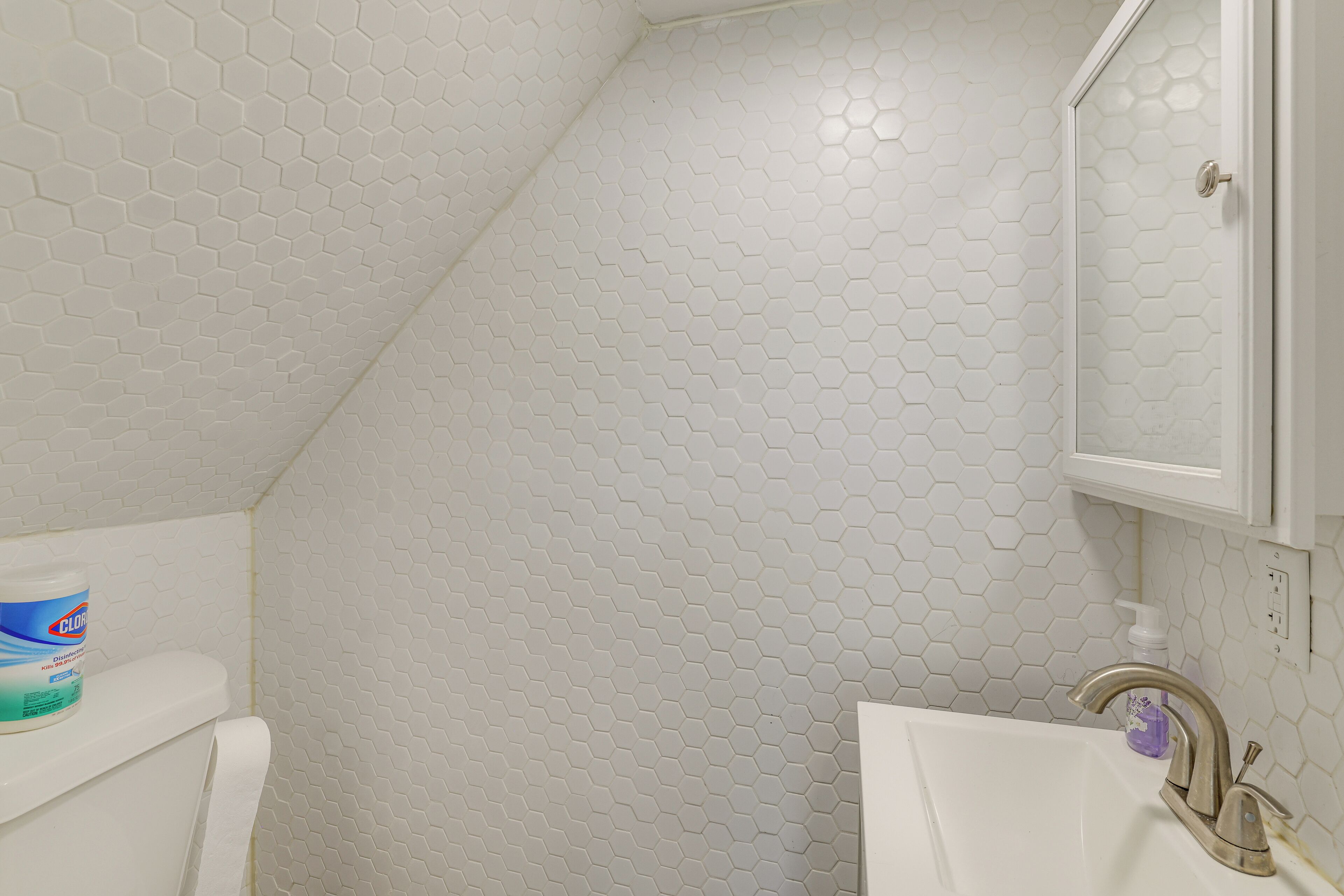 A bathroom with a white hexagonal tile pattern, a toilet, a sink with a faucet, and a cabinet above the sink.