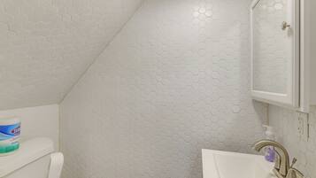 A bathroom with a white hexagonal tile pattern, a toilet, a sink with a faucet, and a cabinet above the sink.