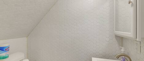 A bathroom with a white hexagonal tile pattern, a toilet, a sink with a faucet, and a cabinet above the sink.