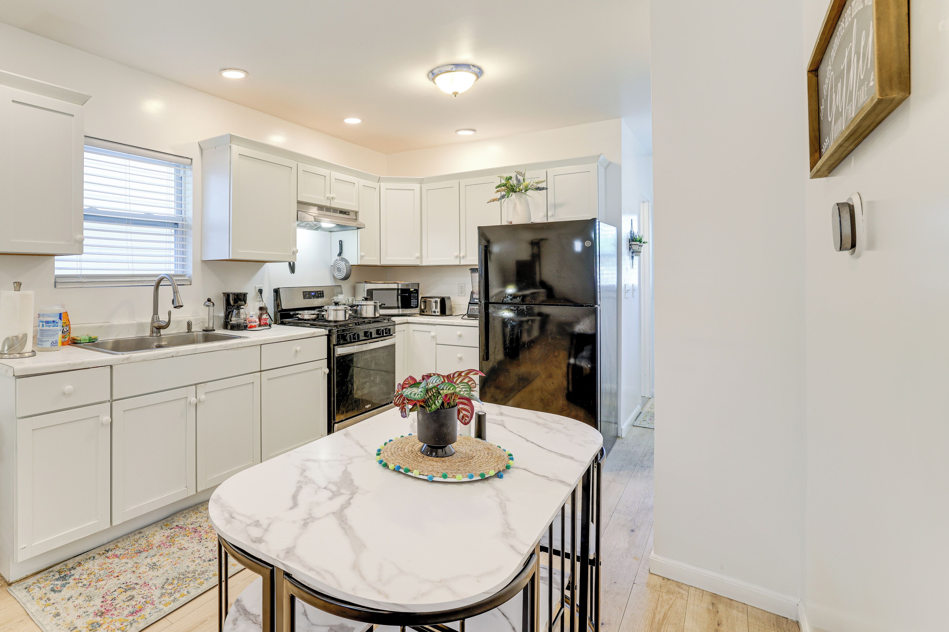 A modern kitchen with white cabinets, a marble countertop, a stainless steel refrigerator, and a central island with a decorative plant.