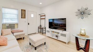 Una sala de estar moderna con un televisor de pantalla plana, muebles blancos y decoración en la pared.