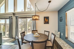A dining area with a round table, chairs, a chandelier, and a view through large windows. - Fairplay Family Cabin on 2 + Acres! 25-0283 (Fairplay)