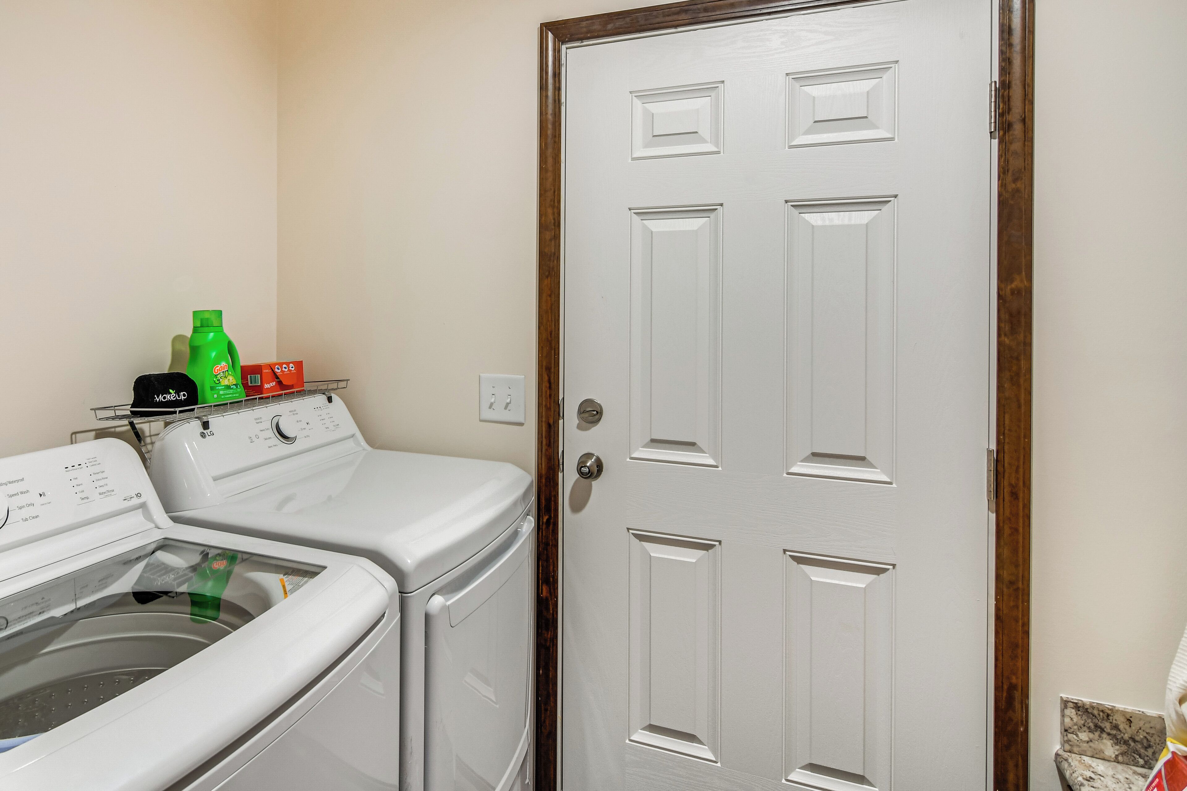 A laundry room with two stacked washers and dryers, a wooden door, and a small shelf with cleaning supplies.