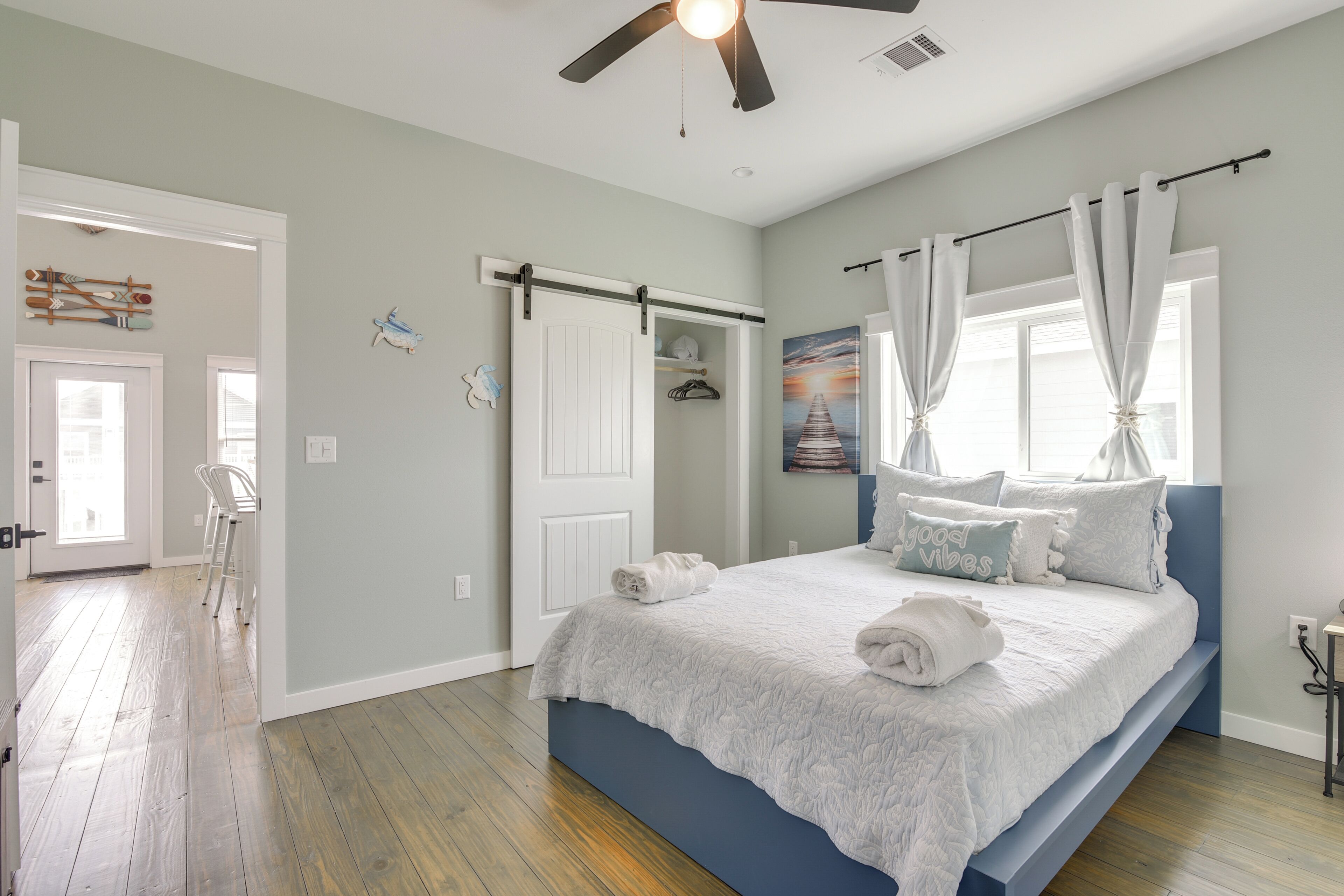 A bedroom with a bed, a ceiling fan, a window with curtains, and a door.