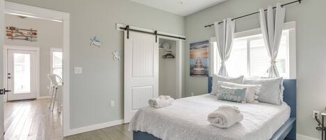 A bedroom with a bed, a ceiling fan, a window with curtains, and a door.