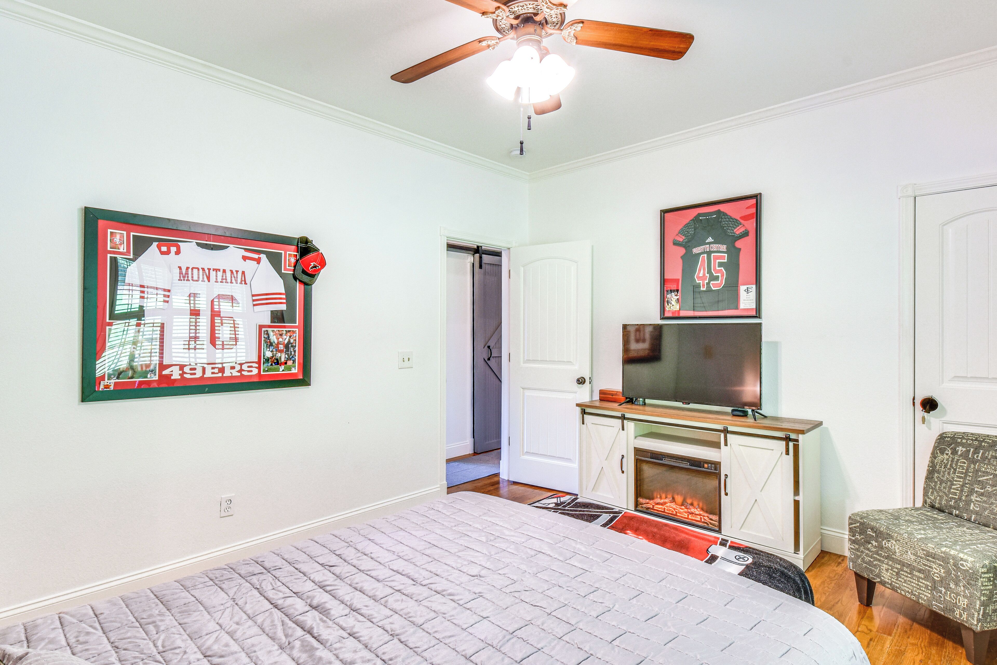 A bedroom with a bed, a ceiling fan, a fireplace, and wall-mounted televisions.