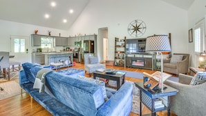 A spacious living room with a large blue sofa, a dining area, and a kitchen with modern appliances. - Hiawassee Cabin Near Lake Chatuge + AT Trailheads (Hiawassee)