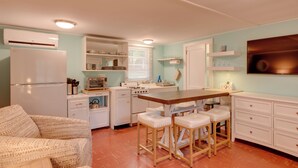 Cocina compacta con electrodomésticos blancos, una zona de comedor con taburetes y un sofá.