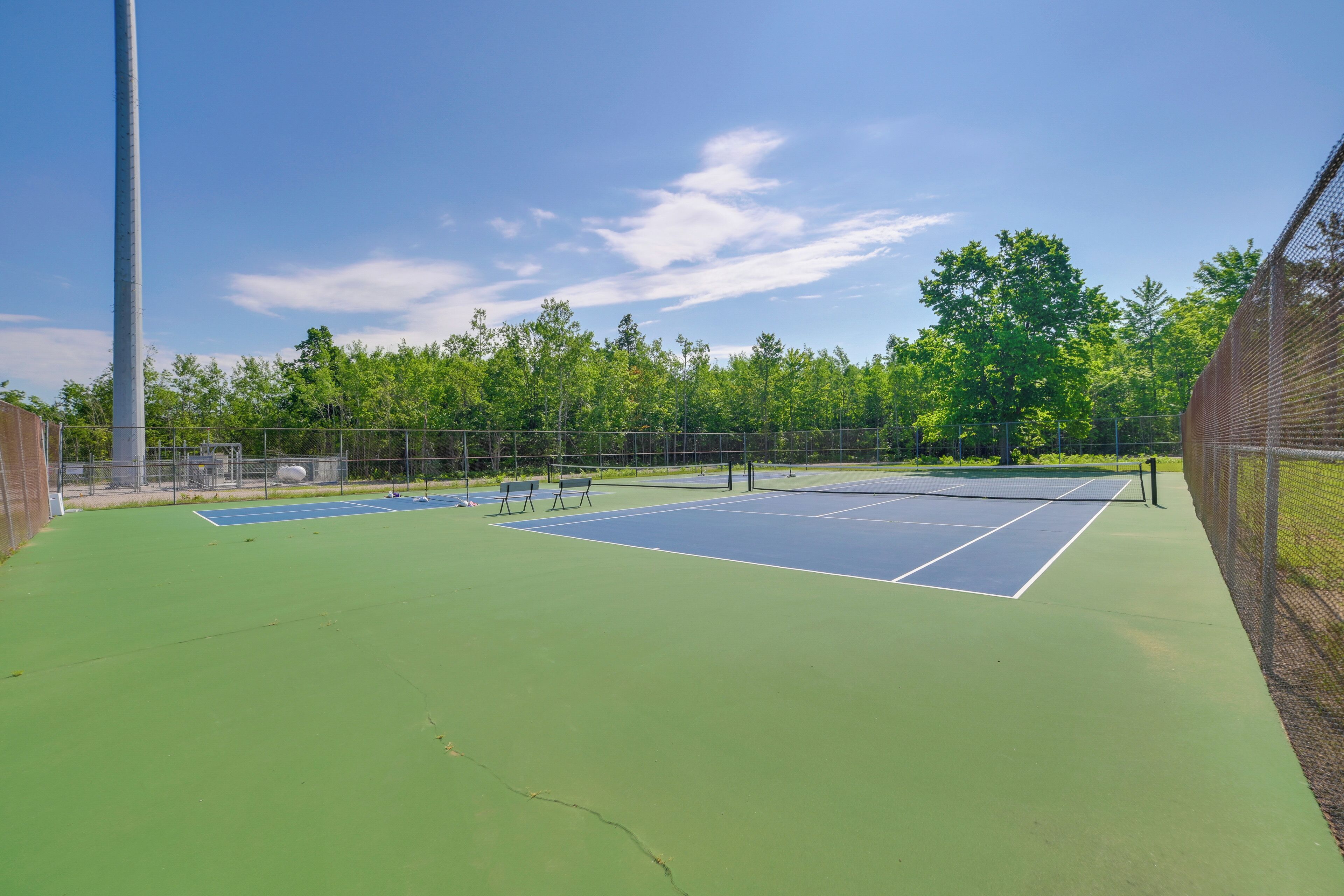 A tennis court with a net, benches, and a fence.