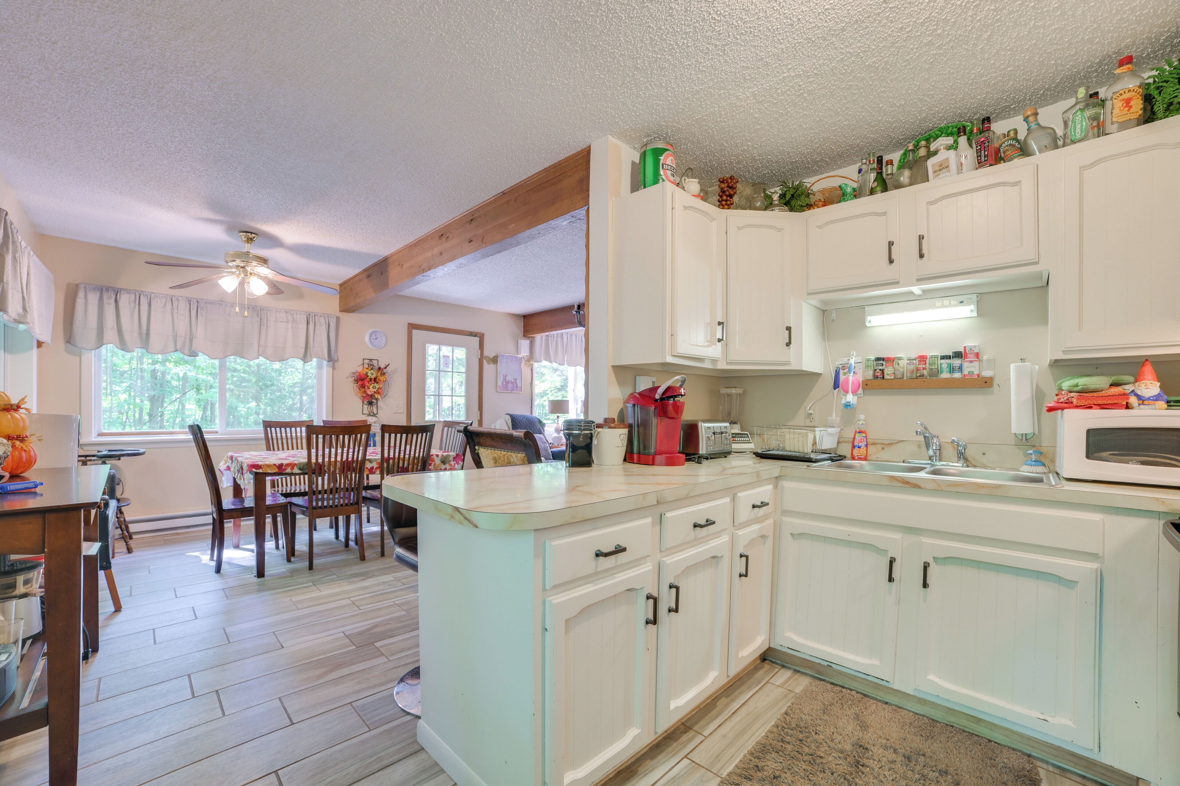 A kitchen with white cabinets, a microwave, and a sink. There is a dining area with chairs and a table.