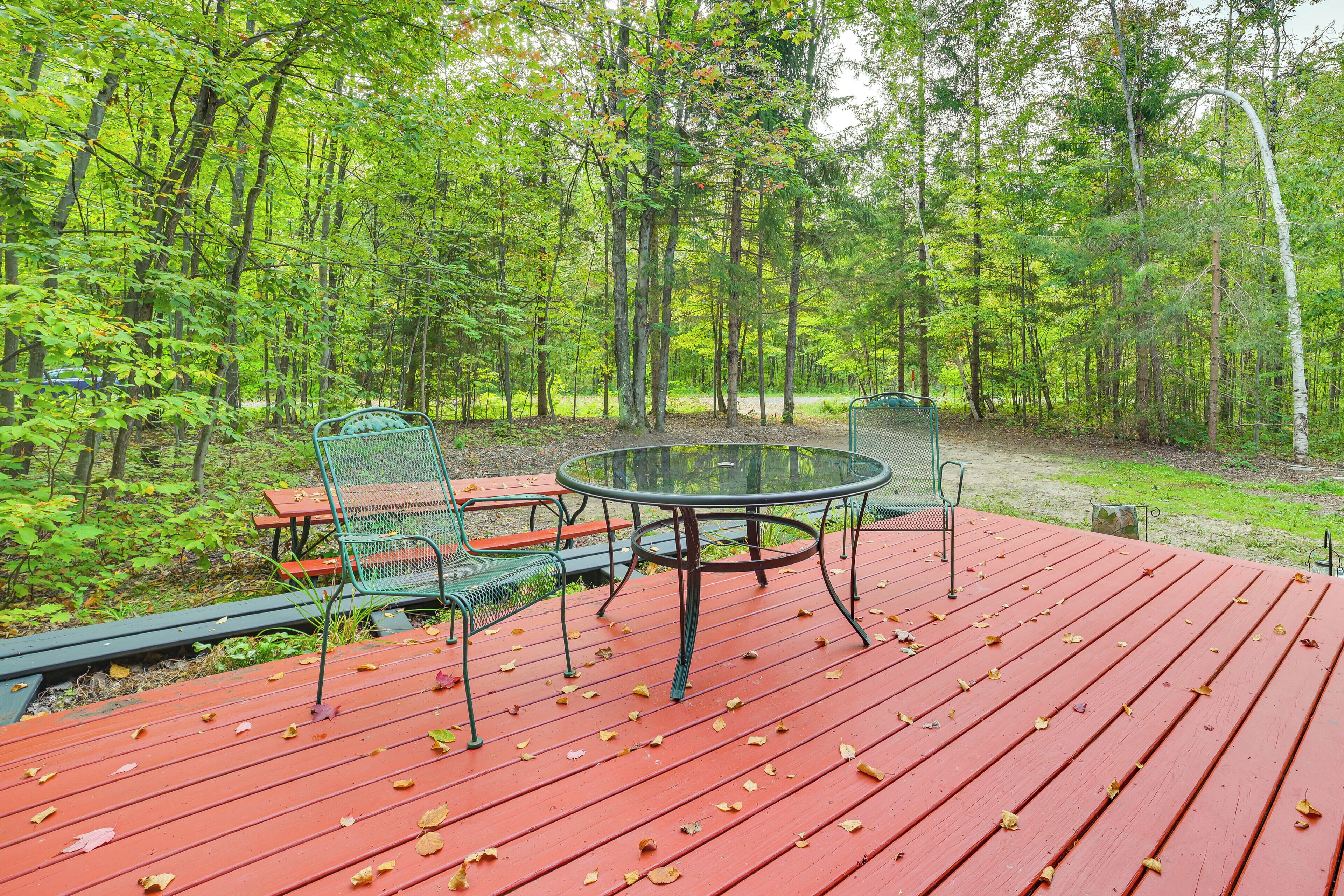 A red deck with a round table and chairs, surrounded by a forest.