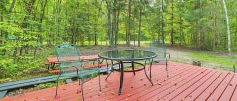 A red deck with a round table and chairs, surrounded by a forest.