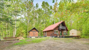 A cabin with a red roof, a wooden deck, and a shed in a forest setting. - Indoor Pool Access: Cabin in Lakes of the North! (Elmira)