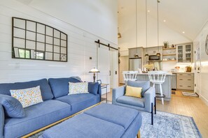 A modern living room with a sofa and ottoman, a kitchen with white cabinets and a bar area, and a large mirror on the wall. - Oregon Wine Country Retreat: Sip & Dine Outside (Sherwood)