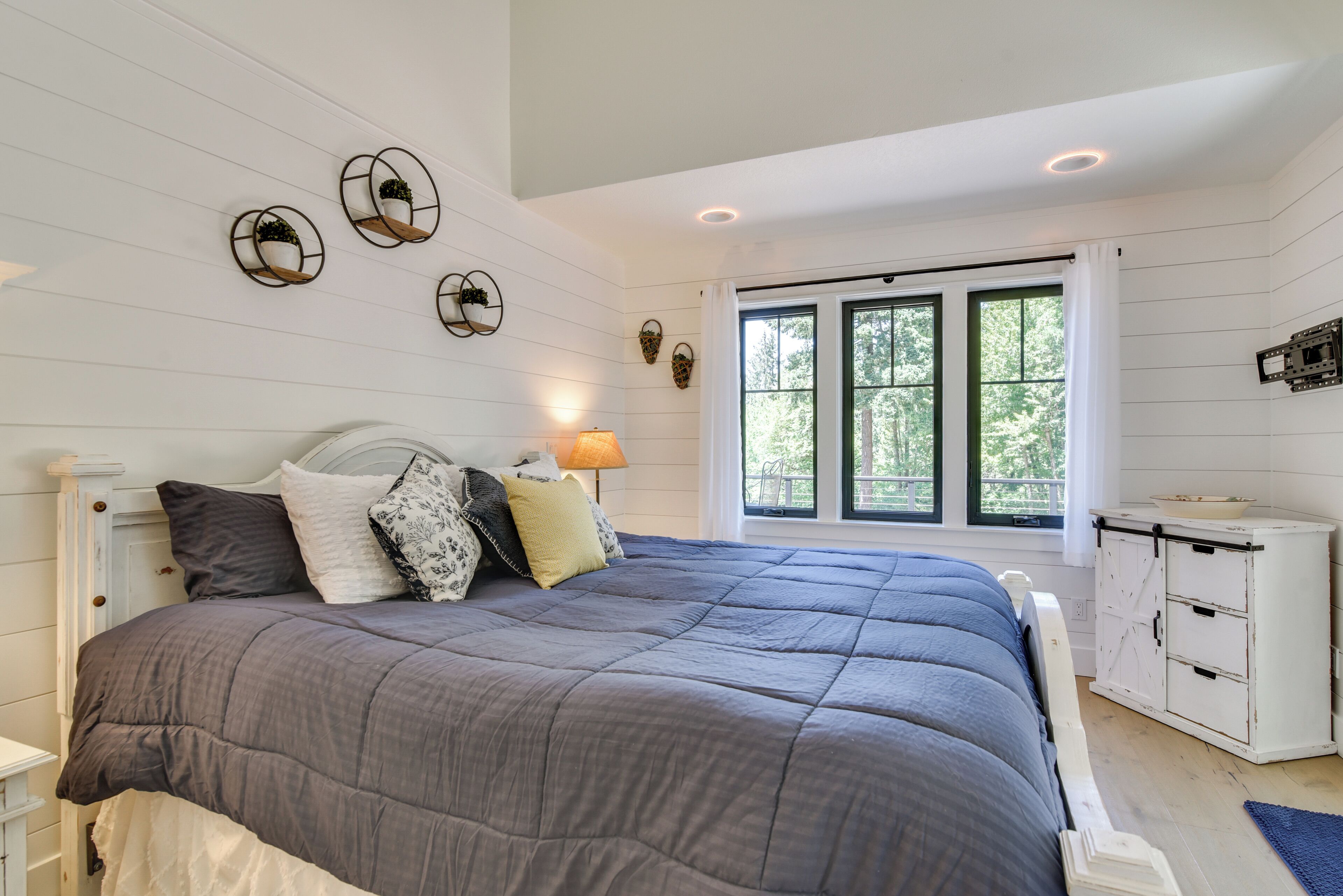 A bedroom with a large bed, a nightstand, a dresser, and a window with curtains.