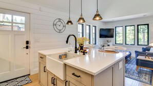 Una cucina moderna con una grande isola, luci a sospensione, un orologio e una TV sullo sfondo.