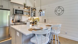 Una cucina moderna con isola centrale, elettrodomestici in acciaio inossidabile, luci a sospensione e orologio a parete.
