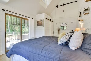 A bedroom with a large bed, a sliding door to a balcony, a round mirror, and a wall-mounted shelf with decorative items. - Oregon Wine Country Retreat: Sip & Dine Outside (Sherwood)