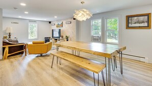 A modern dining area with a wooden table and benches, a sofa, and a television. - Steps to Saco River: Outdoor Rec Hub in White Mtns (Conway)