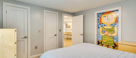 A bedroom with a bed, a painting on the wall, and a door leading to another room.