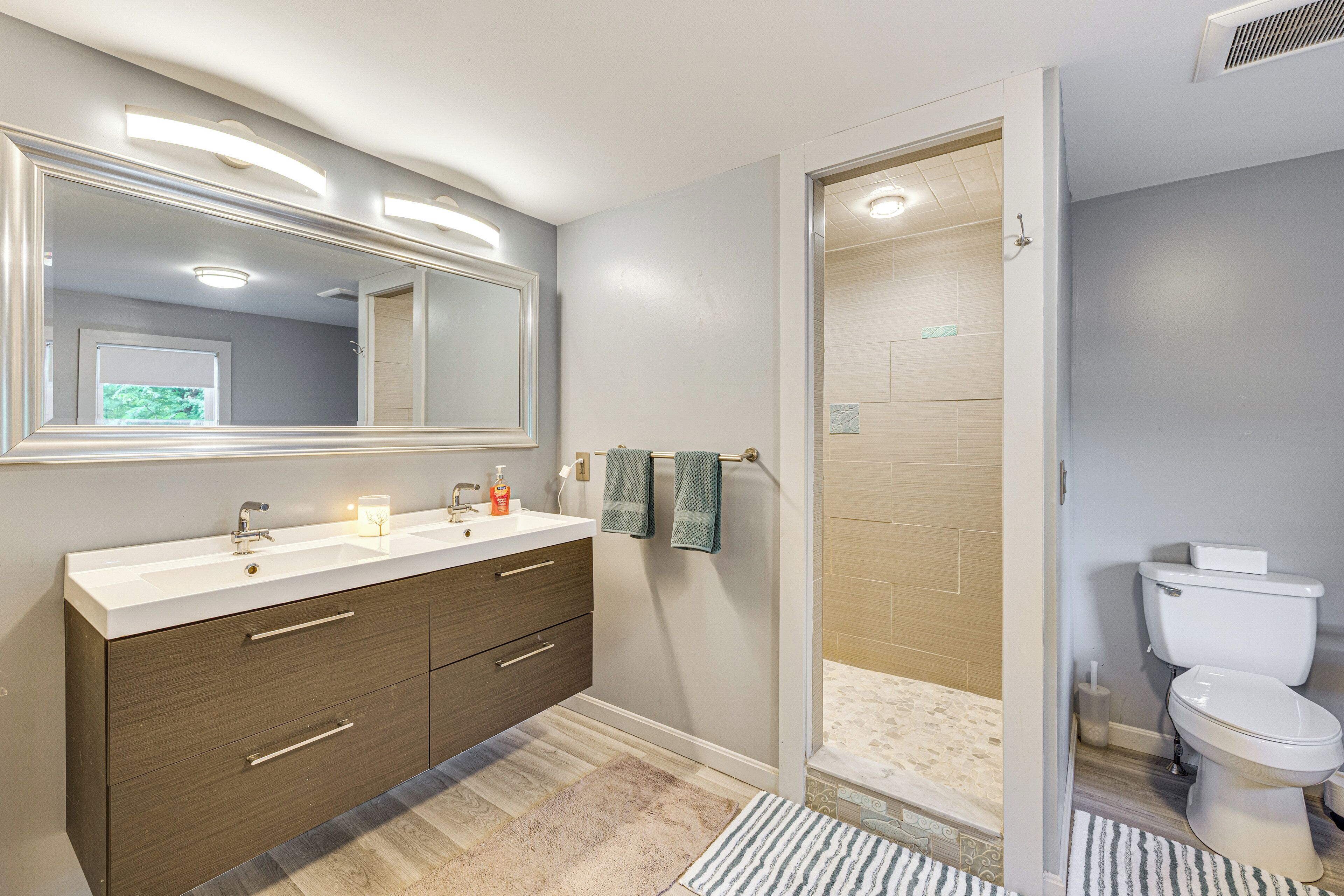 Une salle de bain moderne avec un grand miroir, un meuble-lavabo avec des tiroirs, des toilettes et un espace douche.