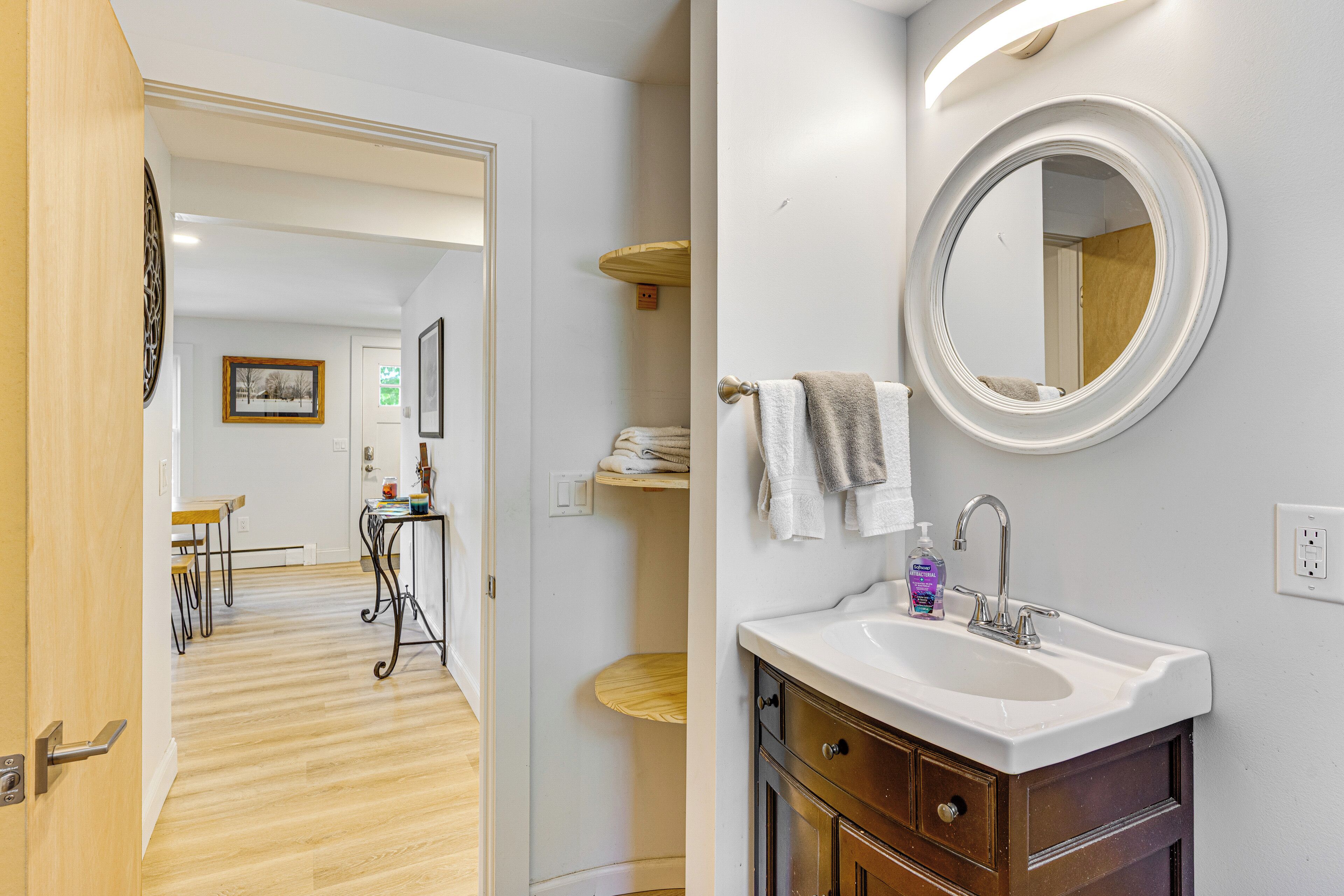 Un baño moderno con un lavamanos blanco, un espejo redondo y un mueble de tocador de madera.