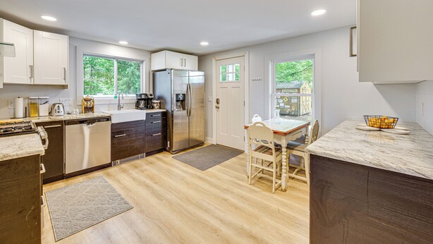 A modern kitchen with white cabinets, stainless steel appliances, and a wooden dining table with chairs. - Steps to Saco River: Outdoor Rec Hub in White Mtns (Conway)