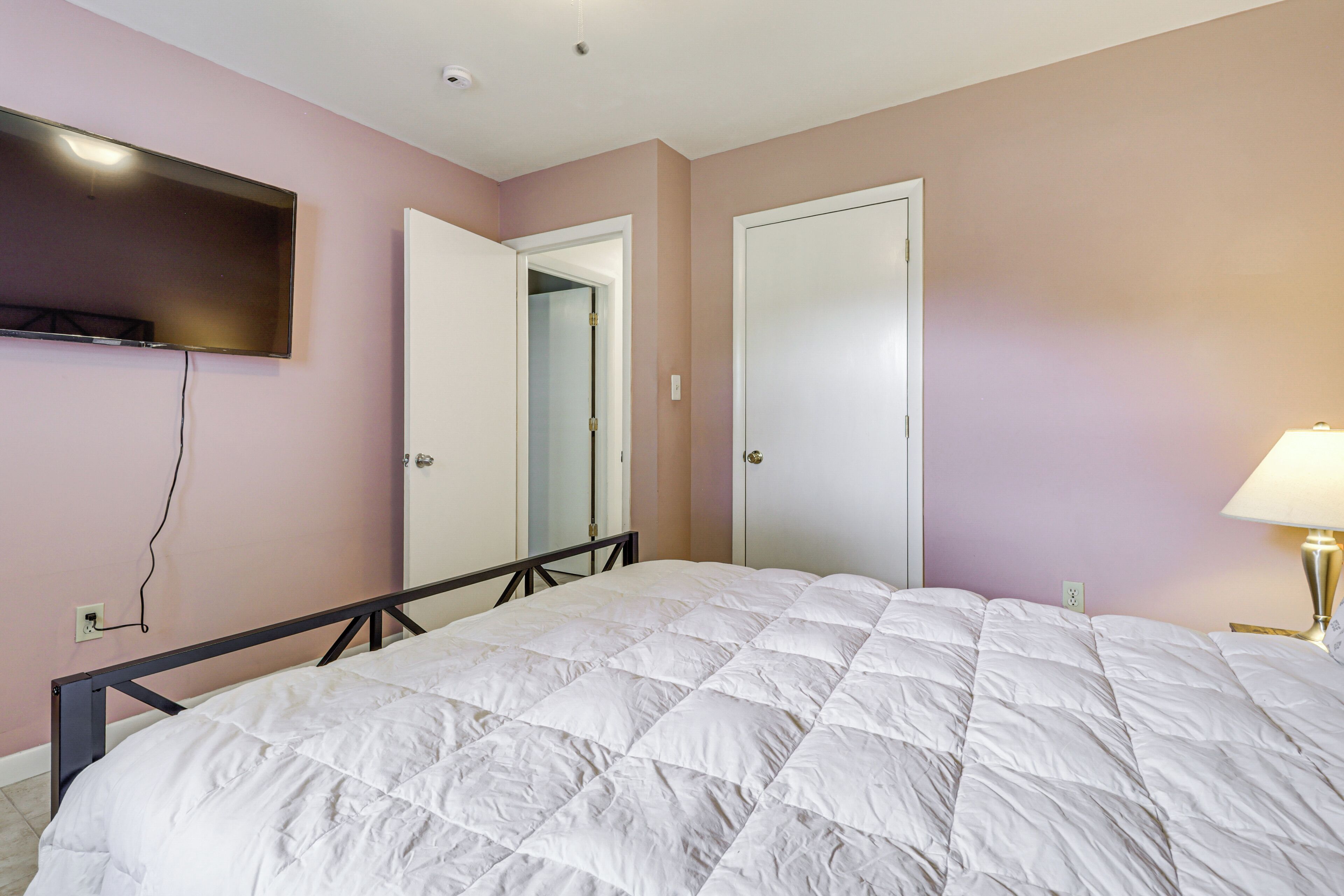 Un dormitorio con una cama, un televisor montado en la pared y una puerta que da a otra habitación.