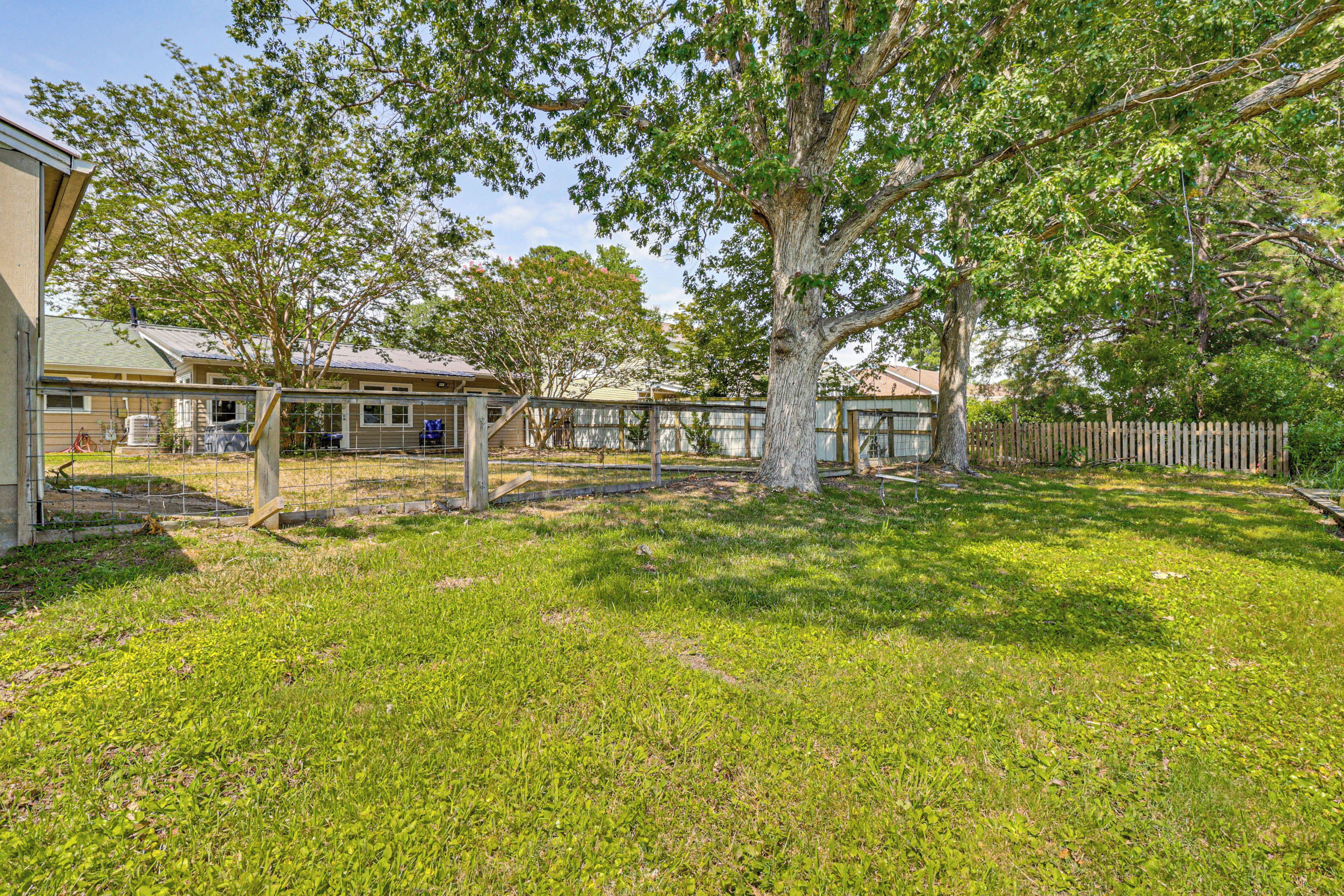 Patio trasero residencial con un árbol grande, zona de juegos cercada y una casa al fondo.
